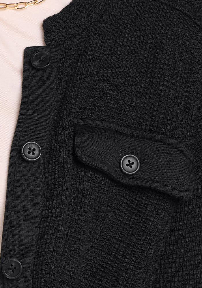 Close-up of the Woolx Oaklynn Waffle Shacket in black, featuring black buttons and a chest flap pocket. Styled over a light top and gold chain necklace for a warm, layered look.