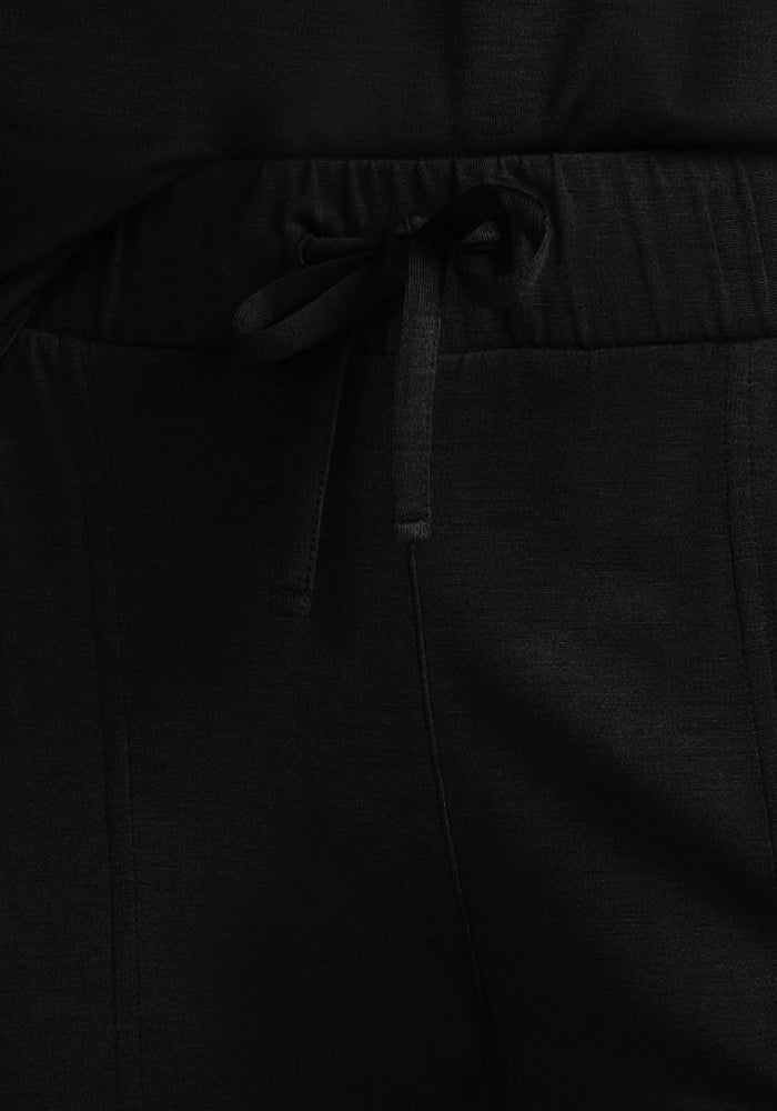 Close-up of Woolx Mary Kate Lounge Pants in black Merino wool. Features a drawstring waist, visible stitching, and soft matte texture. Ideal as moisture-wicking travel lounge wear.