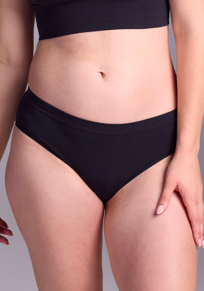 Model wearing the Woolx Maeve Bikini - Black, featuring a seamless bikini bottom and matching top, shown from midriff to upper thighs against a neutral background.