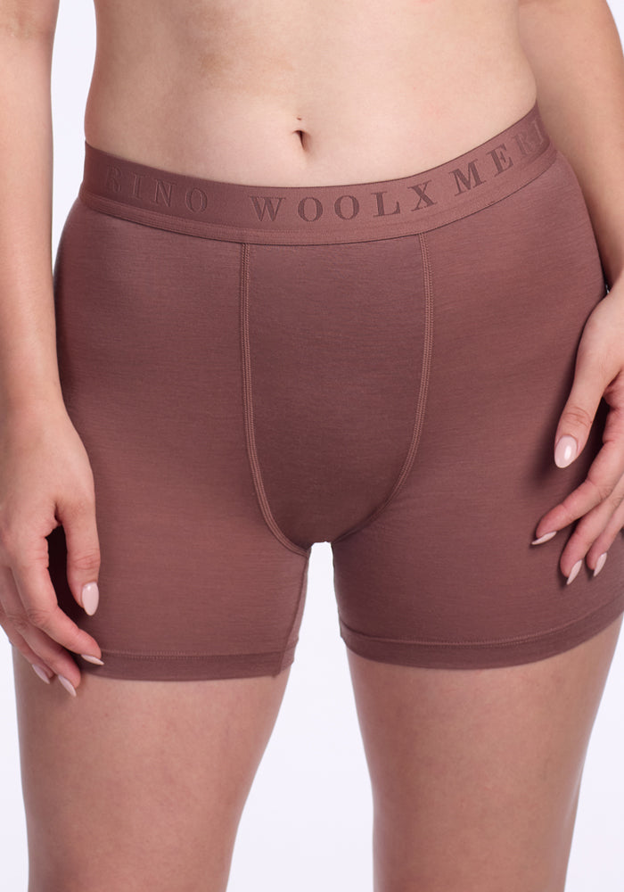 A person wearing Woolx Elliott Boyshort underwear in nutmeg, featuring "WOOLX MERINO" on the waistband, stands against a light background. Only their torso and upper legs are visible.