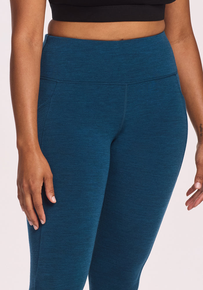 A person models Woolx’s Piper Pocket Leggings in Majolica Blue, paired with a black crop top, standing with arms relaxed by their sides, shown from mid-torso to mid-thigh against a plain background.