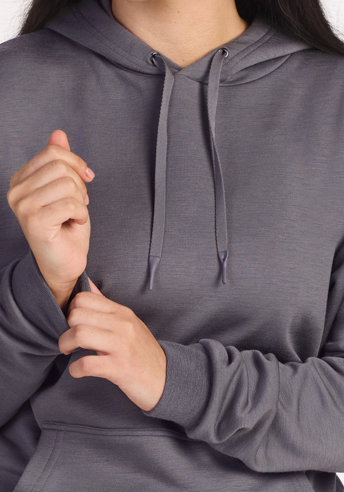 A person wearing the Woolx Avery Hoodie in Arctic Dusk pulls at the sleeve with one hand while the other hand is near their chest, their face partially out of frame, emphasizing this hoodie’s all-season comfort.