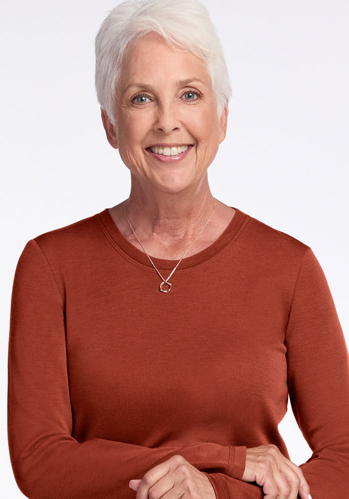 Older woman with short white hair and a warm smile, wearing the Woolx Blair Tunic in Maple Leaf and a simple necklace, standing against a plain light background.