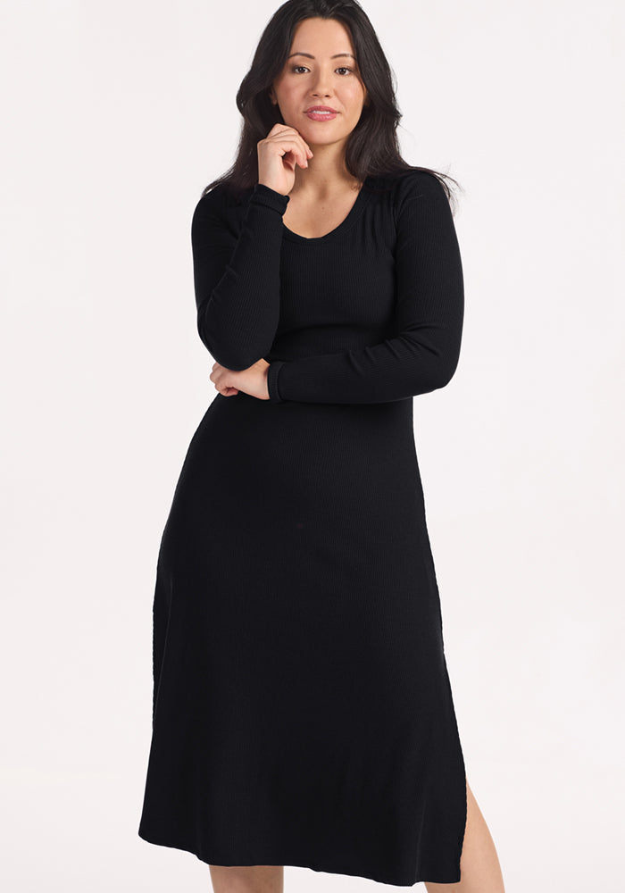 Woman in Woolx Caroline Ribbed Twirl Dress - Black poses with hand on chin against a white backdrop.