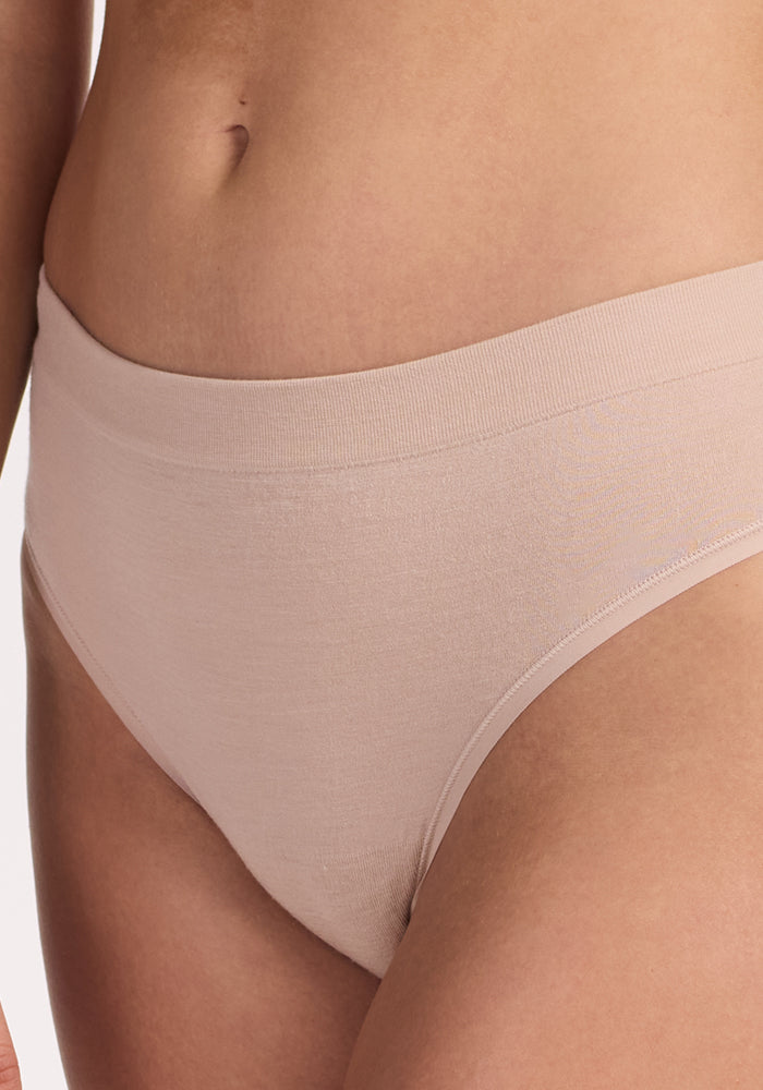 Close-up of a person wearing the Woolx Maeve Bikini in Sand, a high-waisted, seamless nude shade underwear, highlighting the lower torso and hips against a plain background.