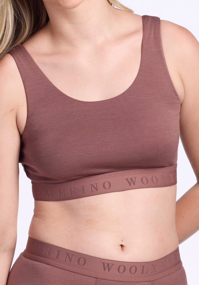 A person wearing the Woolx Aubrey Lounge Bra in Nutmeg, featuring a logo band, shown from the shoulders to just above the waist.