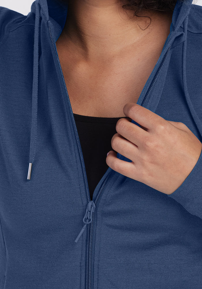 A person in the Woolx Ryann Hoodie - Starry Night is partially unzipping it over a black top, hand on the zipper. Their face isn’t shown; this travel essential delivers comfort and style wherever you go.