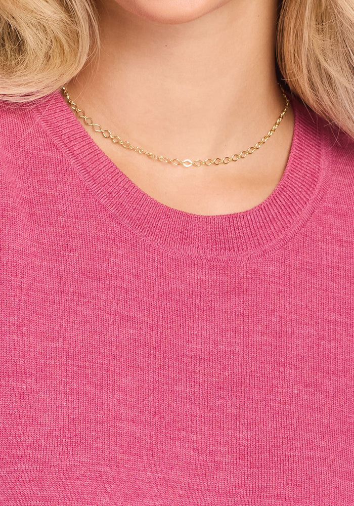 A close-up of a person wearing a simple gold chain and the Woolx Anna Crew Sweater in Wild Salmon. Only their neck, part of the chin, and some blonde hair are visible.