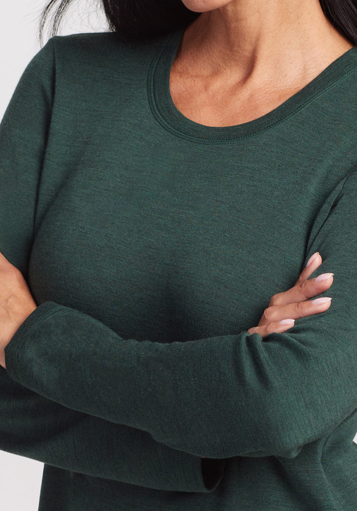 Close-up of a person with long dark hair wearing the Woolx Blair Tunic in Forest, arms crossed. Their face is partially out of frame. This Merino wool tunic provides lightweight warmth for everyday comfort.