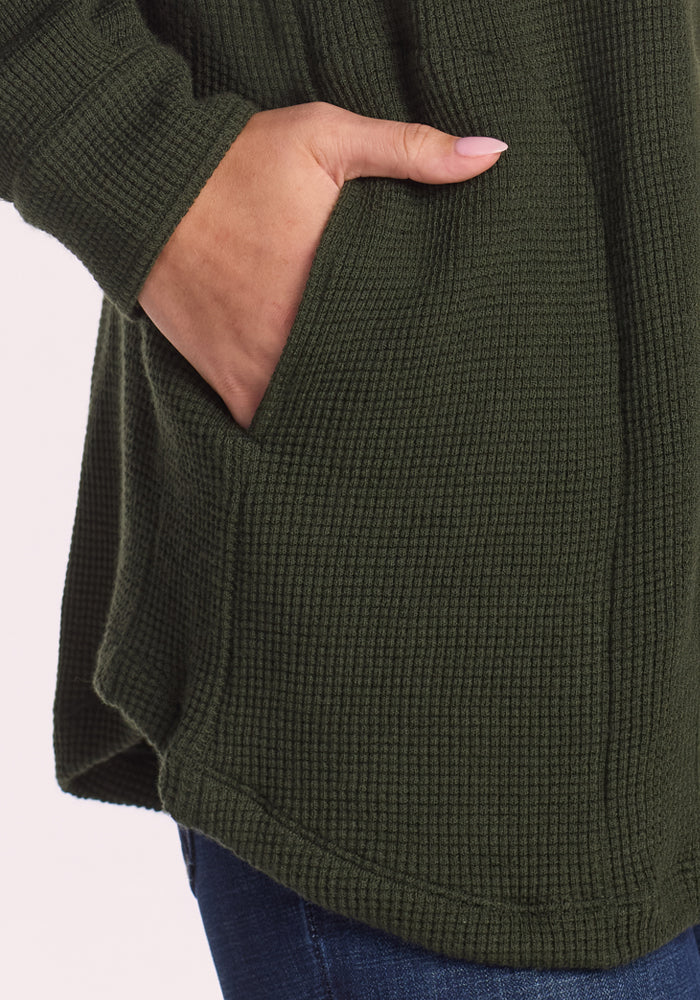 A close-up of someone in the Woolx Oaklynn Waffle Shacket - Driftwood Fern, hand in a pocket, highlighting its textured waffle Merino wool and worn with dark blue jeans—an ideal warm layering shirt.