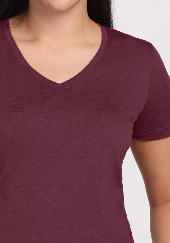 A person models the Woolx Junie V Neck - Grape Harvest, a short-sleeved, moisture-wicking shirt. The image is cropped to show only the lower half of the face, neck, shoulders, and upper torso against a plain background.