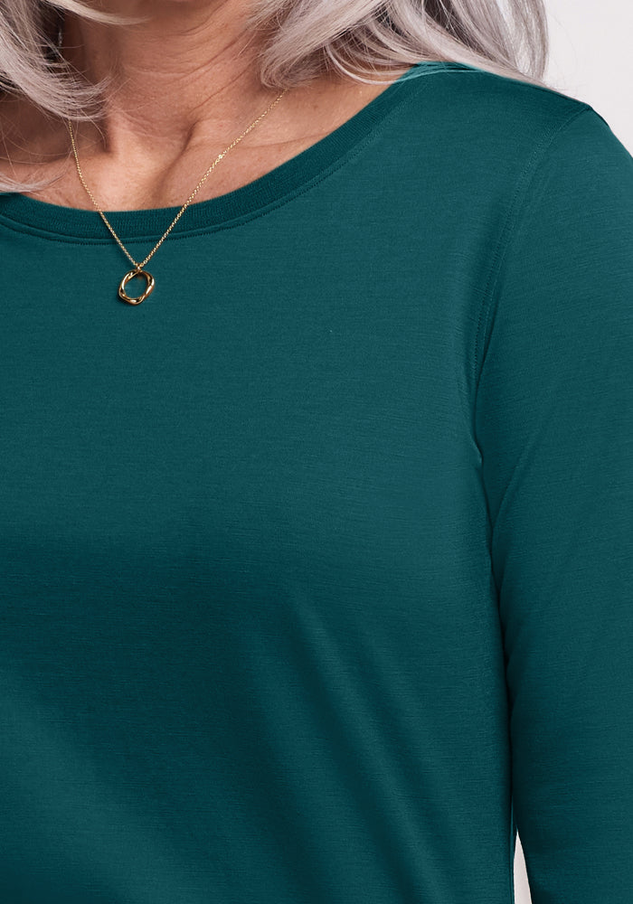 A close-up of a person with long, gray hair wearing the Woolx Jenny 3/4 Sleeve Crew Neck in Riverbank Green and a gold necklace with a circular pendant.