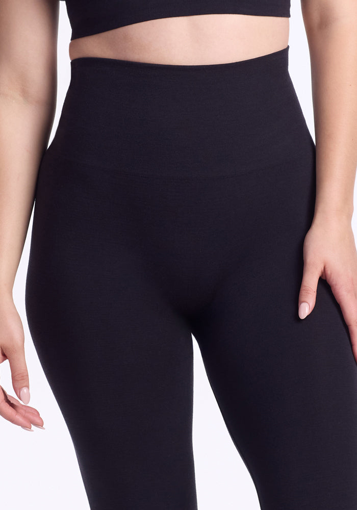A person wearing Woolx Ellis Seamless Tights in black, high-waisted with tummy control, paired with a matching crop top, shown from mid-torso to mid-thigh against a white background.