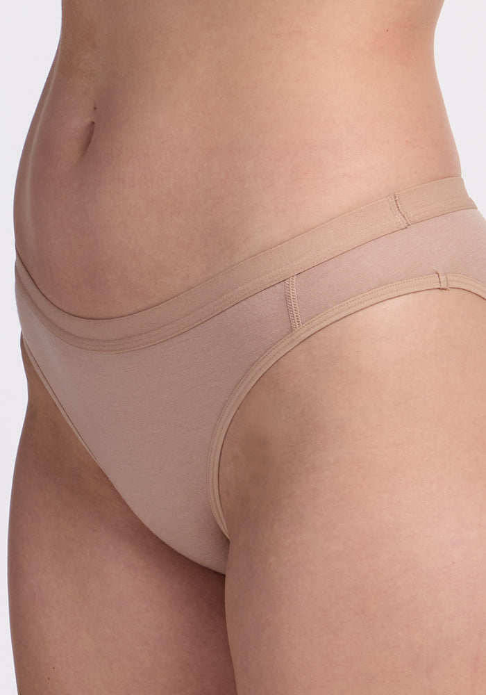 Close-up of a person wearing Woolx Roxie Bikini Underwear in Morning Latte, showing the side and front waist and hip against a plain background.