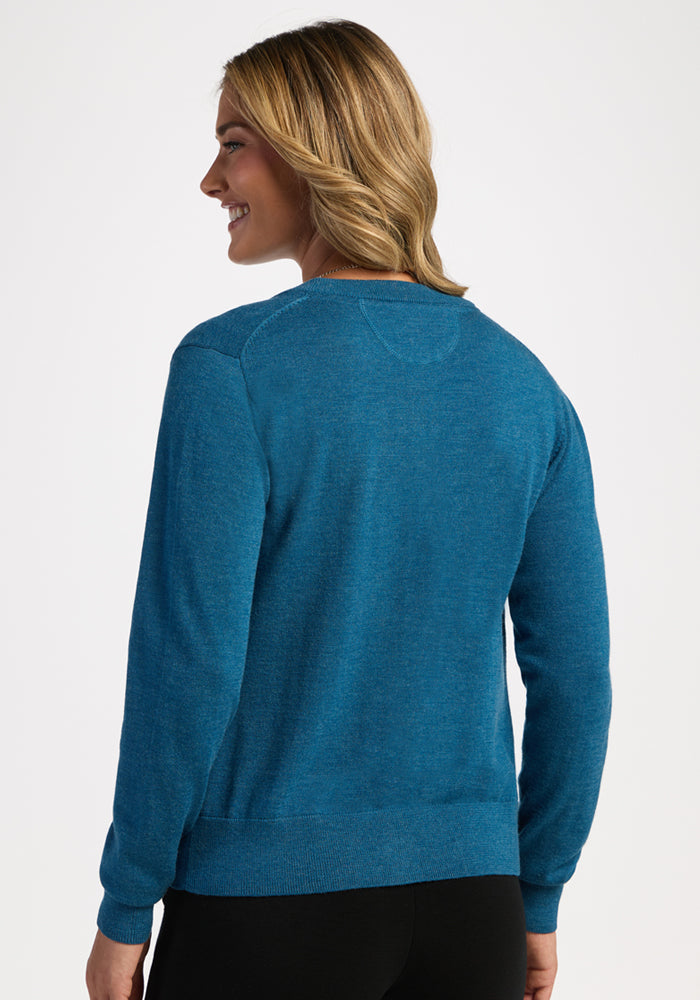 Smiling person with long, wavy hair in a blue Woolx Caitlin Sweater, seen from the back and looking left.