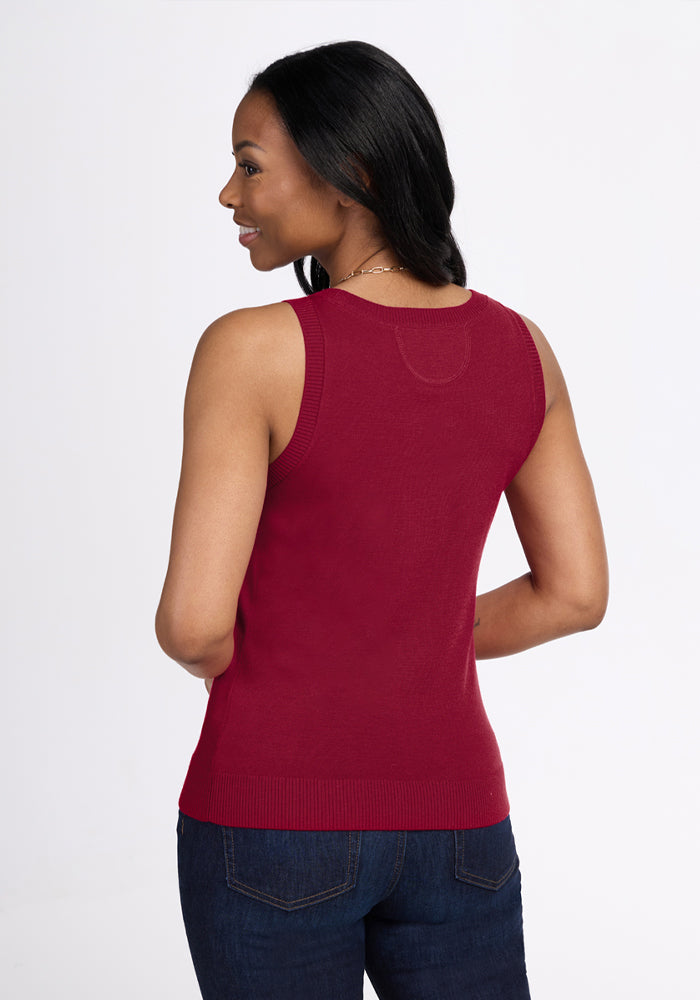 Woman in Woolx Chessy Tank Top - Beet Red, smiling, standing with her back to a white backdrop and dark jeans.