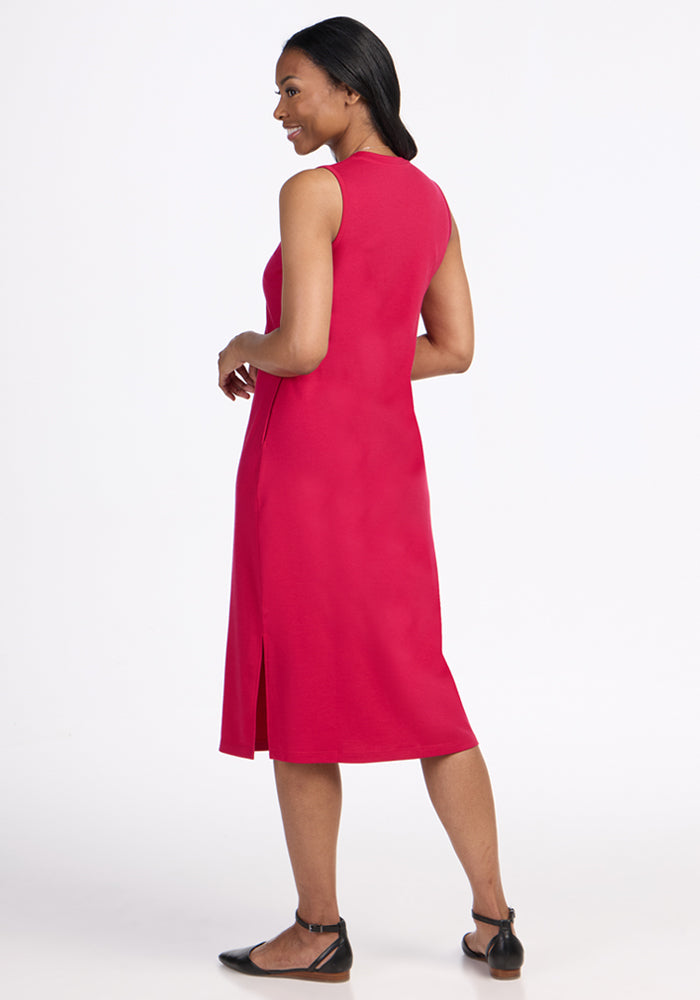 A woman with dark hair pulled back models the Woolx Cassie Dress in Poppy Spark, paired with black flats, as she stands facing away against a plain white background.