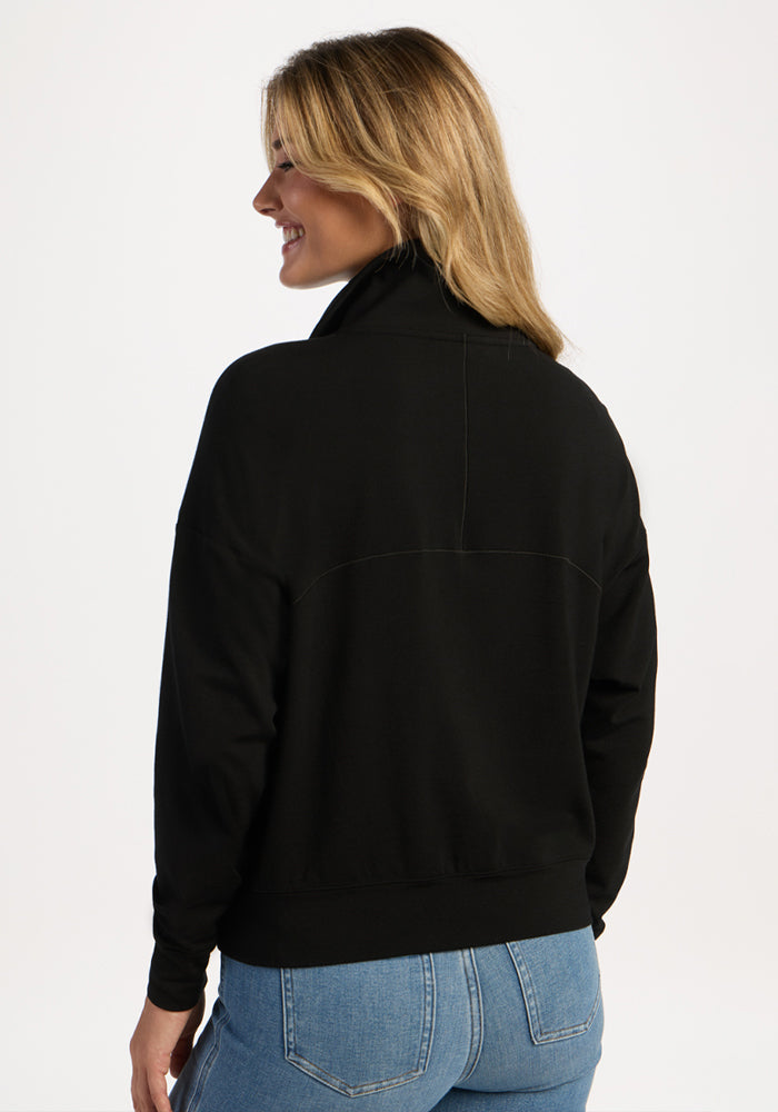 Back view of a woman wearing a black Woolx Tori 1/4 Zip pullover and blue jeans.