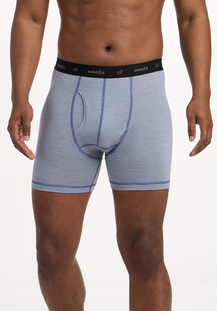 A person wears Woolx Reaction Boxer Briefs - Blue Sand Mini Stripe, featuring a black "Woolx" waistband, standing against a white background. Only the torso and upper legs are shown, highlighting this comfortable underwear. 