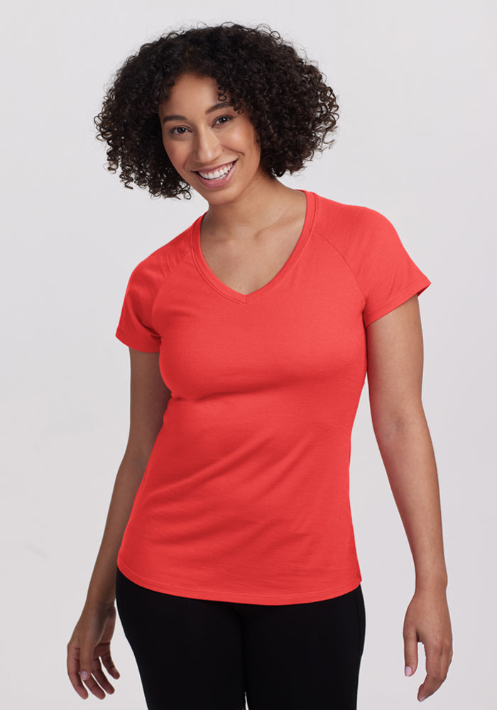 Smiling woman with curly hair wears Woolx Mia V Neck - Hibiscus and black pants, looking at the camera. 