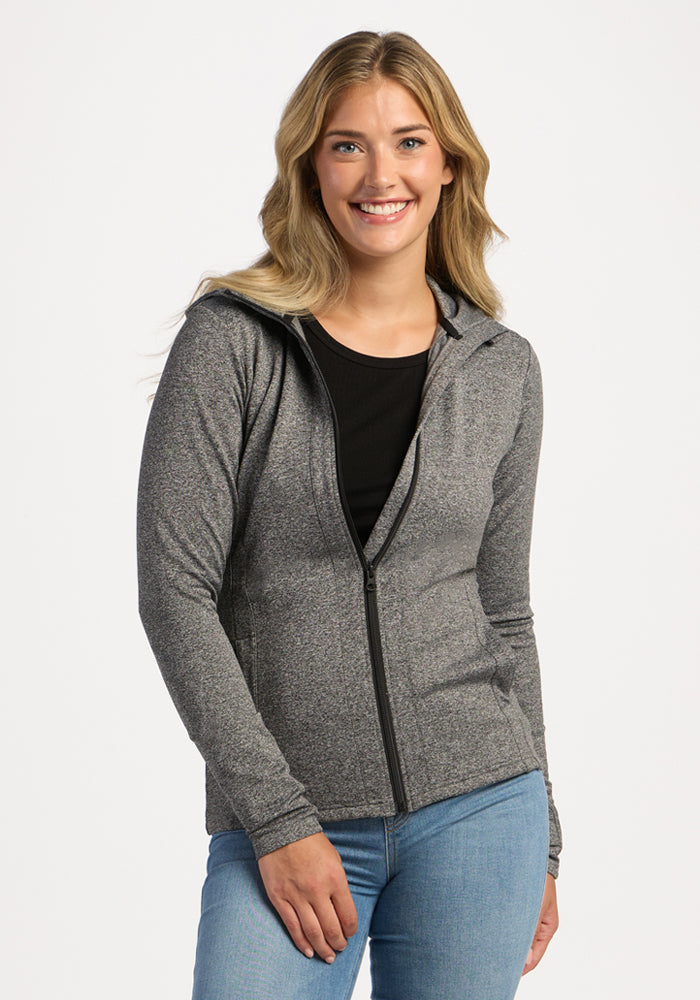Smiling woman in Woolx Zoey Zip Up Hoodie - Thunder Melange and blue jeans stands against a white background.