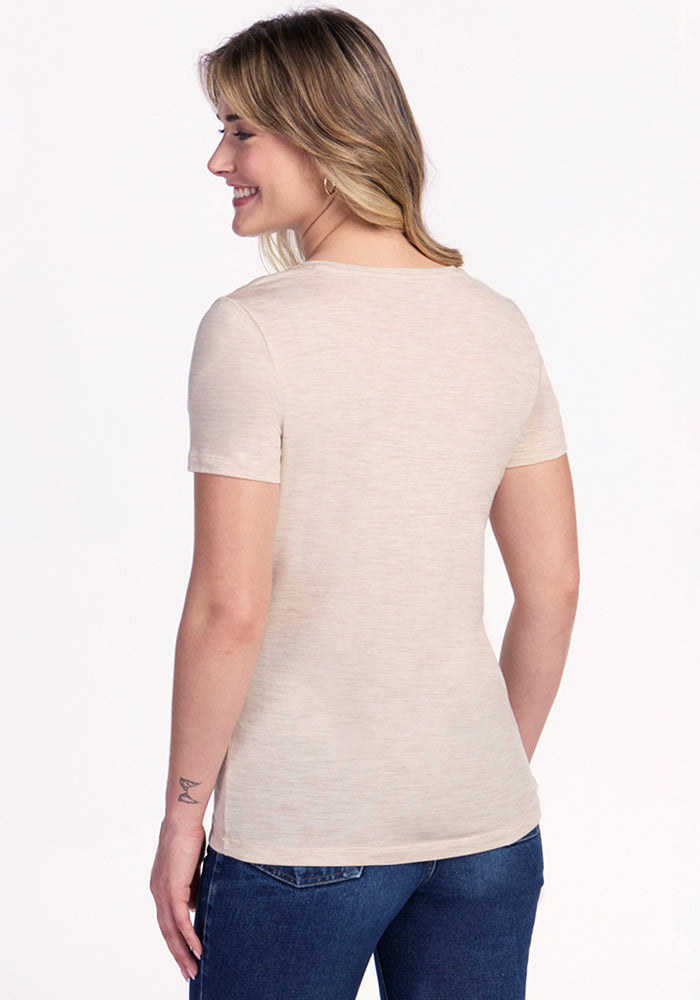 A woman with shoulder-length blonde hair smiles as she faces away from the camera, wearing the Woolx Junie V Neck in Cream Heather with blue jeans against a plain white background.