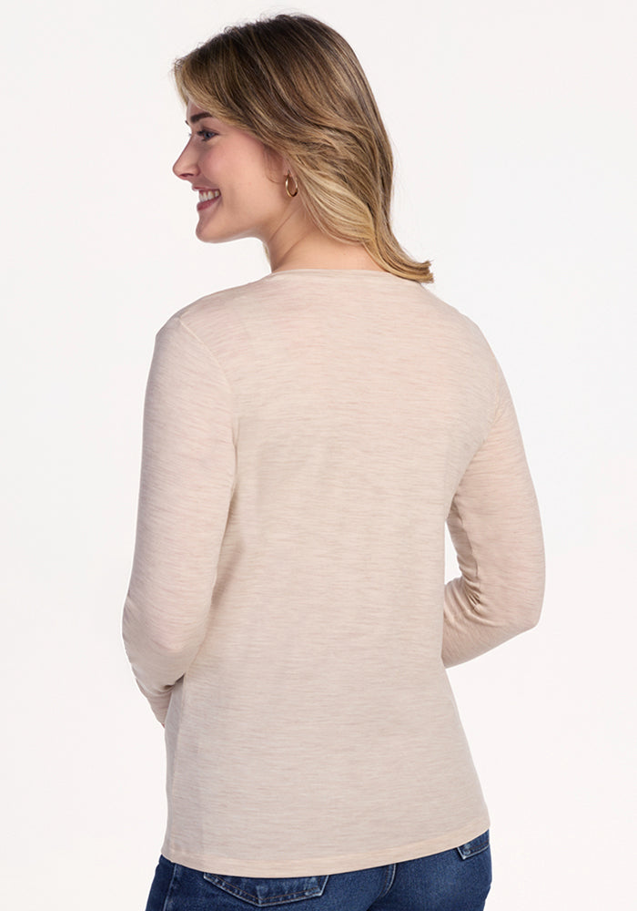 A woman wearing the Woolx Millie Long Sleeve in Cream Heather and blue jeans stands with her back to the camera, smiling over her shoulder against a plain white background.
