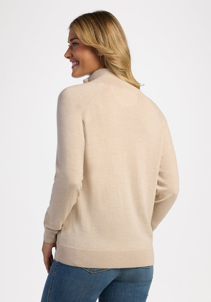 Woman in Woolx Collins Half Zip Sweater - French Oak, blue jeans, smiling over her shoulder against a white background.
