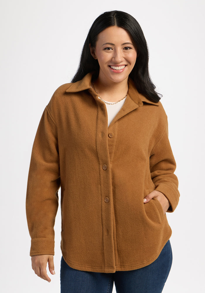 Smiling woman in Woolx Jovie Shacket - Saddleback, hands in pockets, posing against a plain white backdrop. 