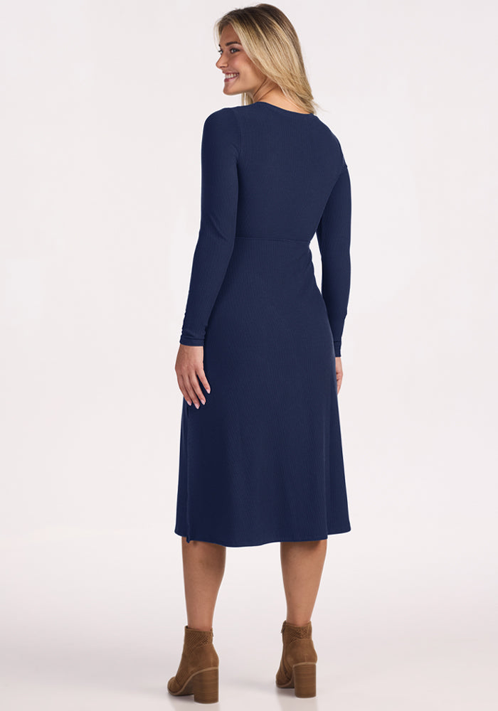Woman in a Woolx Caroline Ribbed Twirl Dress - Ocean Cavern and brown ankle boots, smiling, facing away.