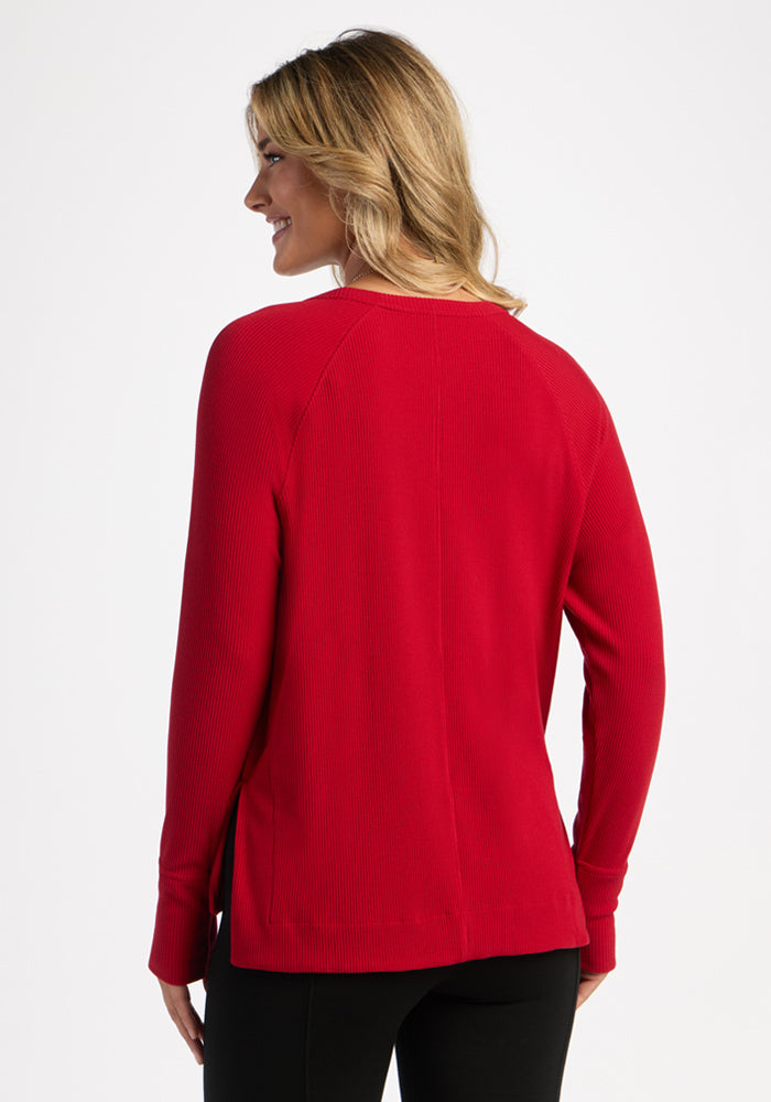 Woman in Woolx Ainsley Sweater - Maraschino Cherry and black pants, shown from the back, smiling and looking aside.