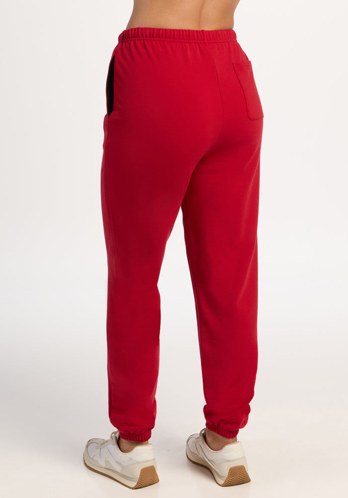 Model wears Woolx Juliette Joggers in Maraschino Cherry with red and white sneakers, shown from the back.