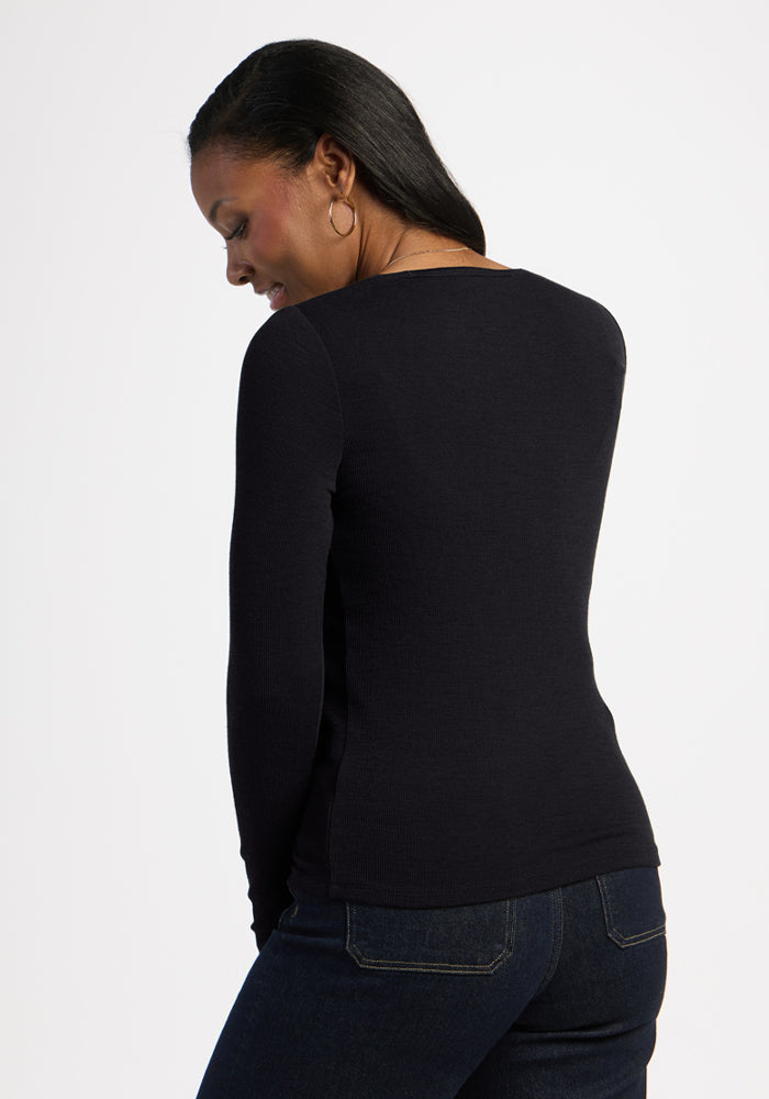 Woman with long dark hair wears the Woolx Katie Ribbed Long Sleeve in black, paired with jeans, facing away and smiling.