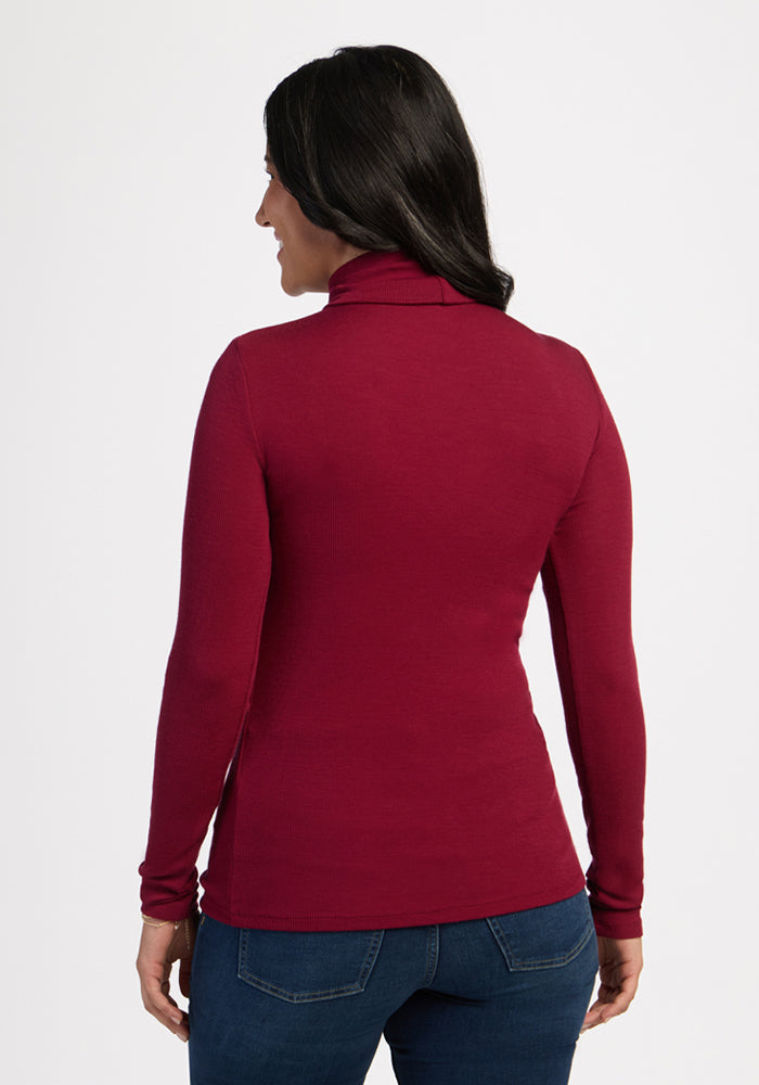 Woman with long dark hair wears a Woolx Sage Ribbed Turtleneck in Beet Red and blue jeans, facing away.