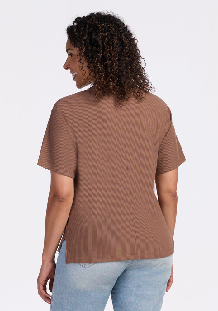 A woman with curly hair stands with her back to the camera, wearing the Woolx Delia Ribbed Short Sleeve in Sienna Kiss and light blue jeans against a plain white background.