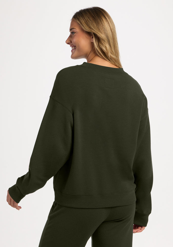 A woman seen from behind wearing an olive green Molly Crewneck - Duffel Bag merino wool sweatshirt.