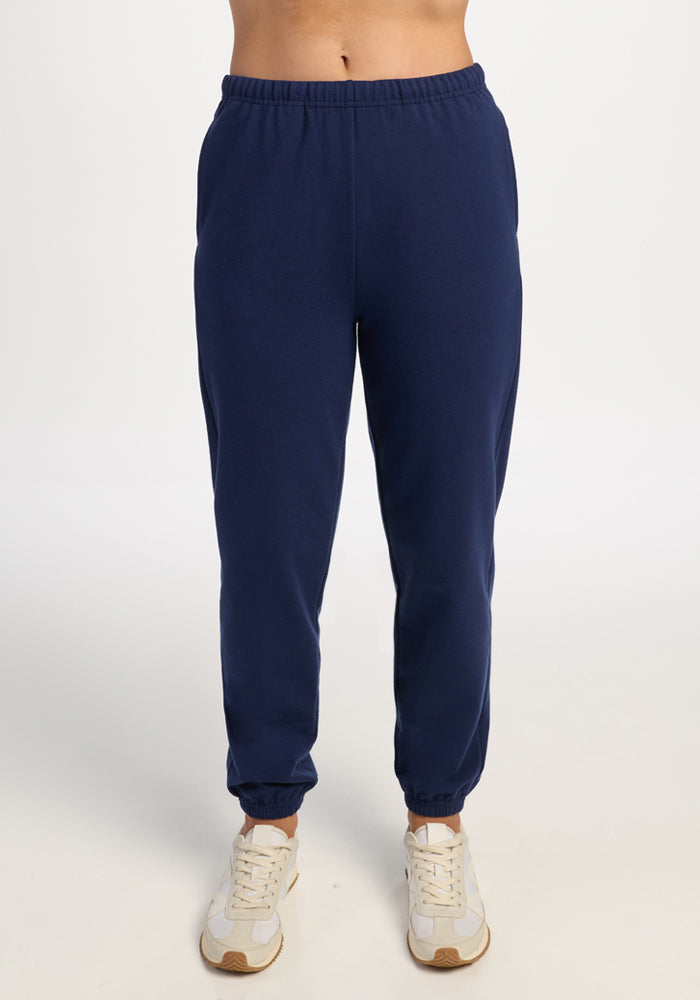 Person wears Woolx Juliette Joggers - Ocean Cavern and white sneakers, standing against a plain white background. 