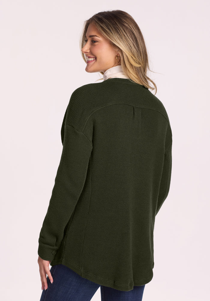 Smiling woman in Woolx Oaklynn Waffle Shacket - Duffel Bag and jeans stands turned, looking over her shoulder.
