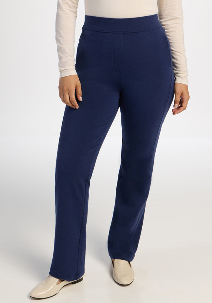 Model wears Woolx Emerson Straight Leg Pants in Ocean Cavern, a white long-sleeve top, and cream shoes on plain backdrop.