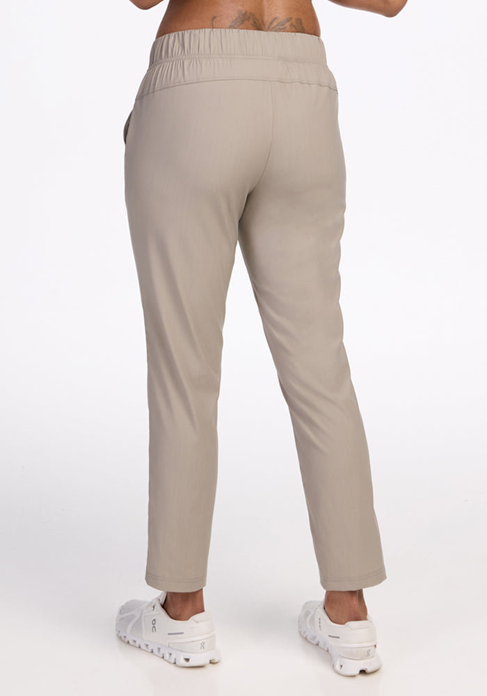 A person wearing Woolx Nicole Ankle Pants in Vintage Khaki, featuring an elastic waistband and a tapered fit, stands with their back to the camera against a plain white background.