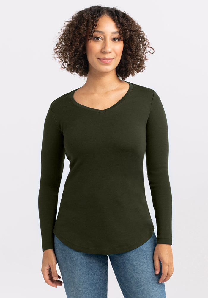 Woman with curly hair wears a Woolx Eva Tunic - Duffel Bag and blue jeans, standing against a light background. 