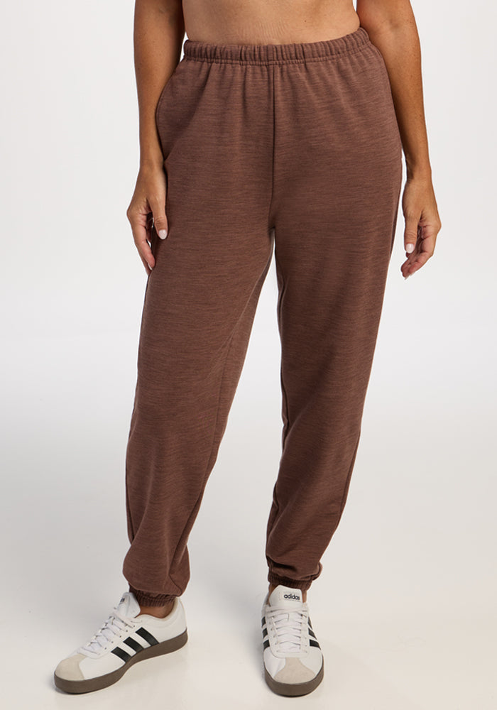 Person wearing Woolx Juliette Joggers in Sable Heather and white sneakers with black stripes, on a white background. 