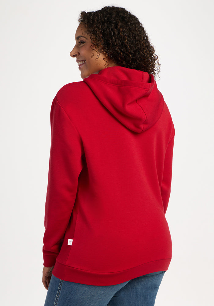 Someone in a Woolx Avery Hoodie - Maraschino Cherry and blue jeans smiles, back to camera, on a white background.