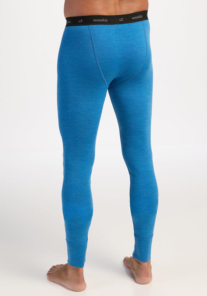 A person stands barefoot, facing away, in Woolx Backcountry Leggings—Blue Razz with a black “woolx” waistband.