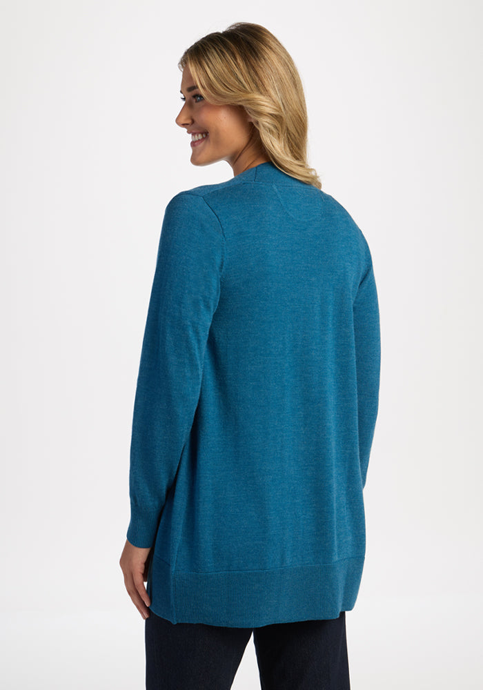 Smiling woman models the Woolx Macie Sweater in Blue Pine, turned to show the back, against a white background.