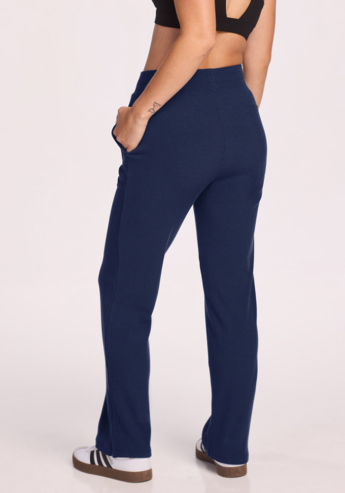 Woman in Woolx Luca Petite Pants - Ocean Cavern, black sports bra, and white sneakers stands with hands in her pockets.