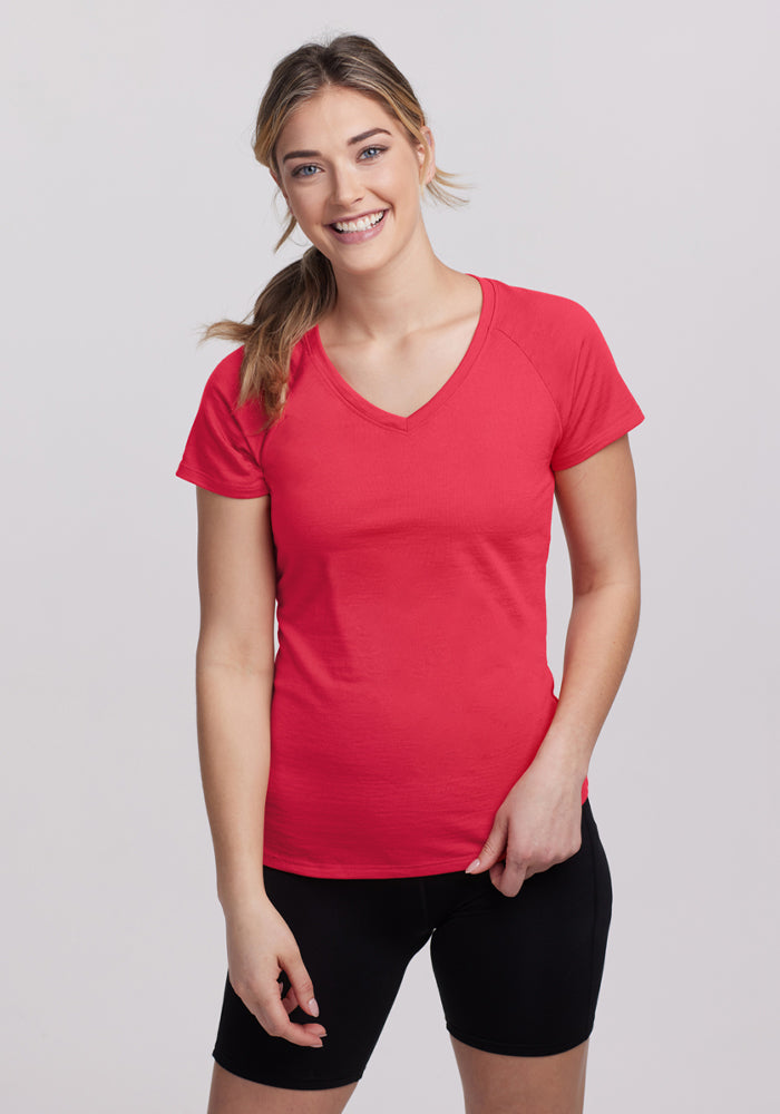 Smiling woman wears the Woolx Mia V Neck in Berry Ice Pop and black shorts against a plain light background. 