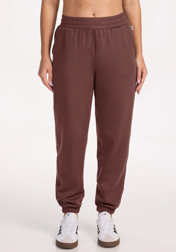 Person in Woolx Parker Sweatpants - Canyon Clay with white sneakers, standing against a plain white background. 