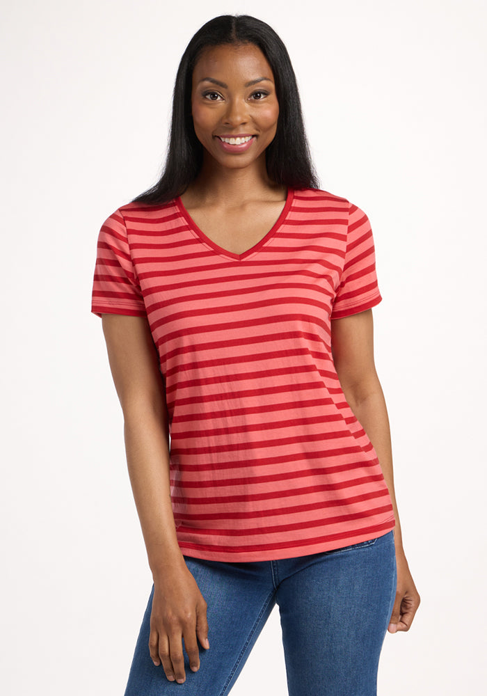 A woman with long dark hair smiles while wearing the Woolx Junie V Neck in Wildberry Stripe and blue jeans, standing against a plain white background. 