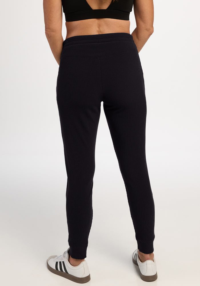 Person wearing Woolx Lennon Ribbed Joggers in black, a crop top, and white sneakers, standing with back to camera.